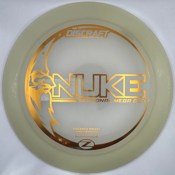 A Discraft Nuke Mega Ball 6.1 disc golf disc, featuring a translucent pale yellow body with a metallic gold foil stamp, shown inside its white protective packaging.