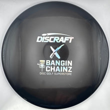 A Discraft Bangin' Chainz disc golf driver photographed inside its white protective packaging sleeve, showing the printed model name and logos on the glossy black face.