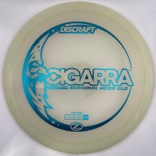 A Discraft Cicarpa disc golf disc in a translucent cream color with a blue graphic design, shown inside its white packaging sleeve.