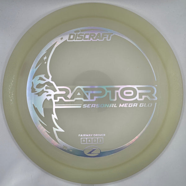 A translucent pale yellow Discraft Raptor Seasonal Med Ball disc golf disc resting on a white foam insert, with a purple surface visible at the right edge.