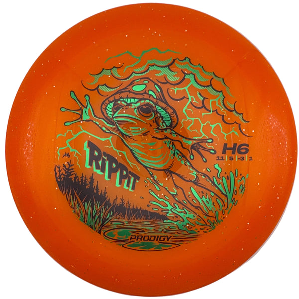 An orange Groovy Rippi H6 disc golf disc with a green and black frog graphic, displayed inside its white presentation box.