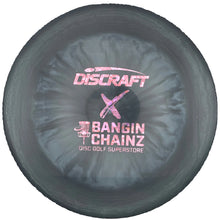 A Discraft Bangin' Chainz golf disc in a dark gray/black finish with pink foil stamping, shown inside its white protective packaging insert.