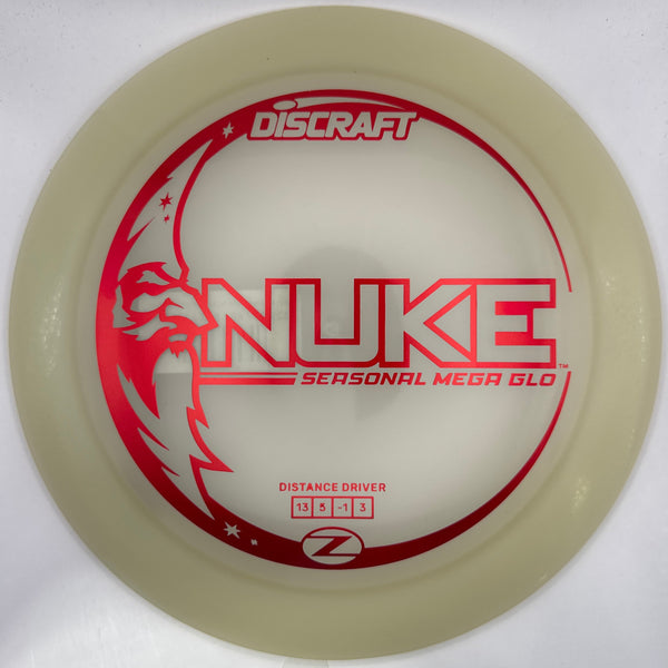 A translucent off-white Discraft Nuke distance driver disc golf disc with red printed graphics and text, resting on a white surface.