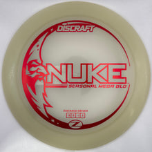 A translucent off-white Discraft Nuke distance driver disc golf disc with red printed graphics and text, resting on a white surface.