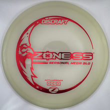 A Discraft Zenness Seasonal Mega Glo disc golf disc in a translucent pale yellow/cream color with red printed graphics and text, resting on a white foam insert.