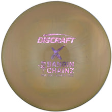 A Discraft Baron Chainz disc golf disc in a translucent tan color, featuring pink foil stamping of the model name and a purple X logo, resting on a white insert.