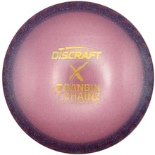 A Discraft X Banrin Chainz disc golf disc in a pink and purple speckled finish with gold foil branding, resting on a white surface.