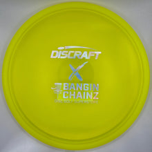 A bright yellow Discraft Bangin' Chainz disc golf disc resting on its white cardboard packaging insert.