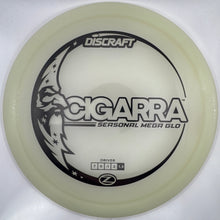 A Discraft Cigarra Seasonal Media Glo disc golf disc in a translucent pale yellow color, resting on its white retail packaging.