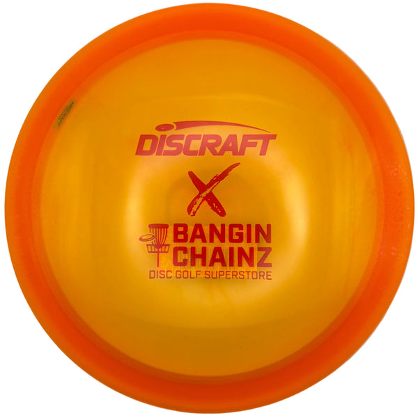 A translucent yellow and orange Discraft disc golf disc with red printed branding, including 'Discraft', 'X', and 'Bangin Chainz Disc Golf Superstore', resting on a white surface.