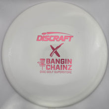 A white Discraft X Bangin' Chainz disc golf disc with pink printed branding, shown inside its white packaging sleeve.