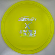 A bright yellow Discraft Bandin Chainz disc golf disc resting on its white cardboard packaging insert.