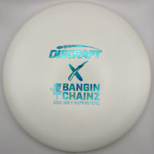 A white Discraft X Bangin' Chainz disc golf disc resting on a white surface with a wooden edge visible at the bottom.
