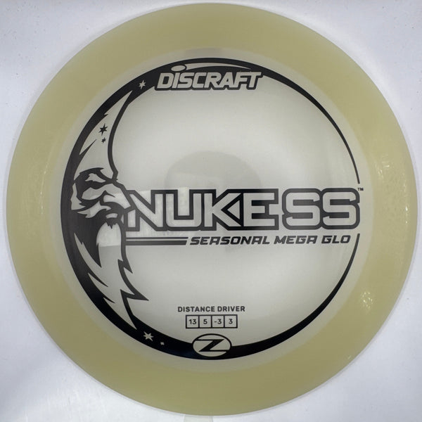 A Discraft Nukess distance driver disc golf disc in a translucent pale yellow color, featuring black printed graphics and text, shown inside its white packaging insert.