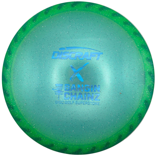 A green and blue translucent Discraft Samin Chairz golf disc with a glitter finish, displayed on a white surface.