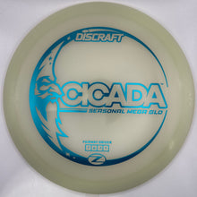A Discraft Cicada Seasonal Meep Glo disc golf disc, featuring a translucent pale green body with blue and white printed graphics, shown inside its white packaging sleeve.