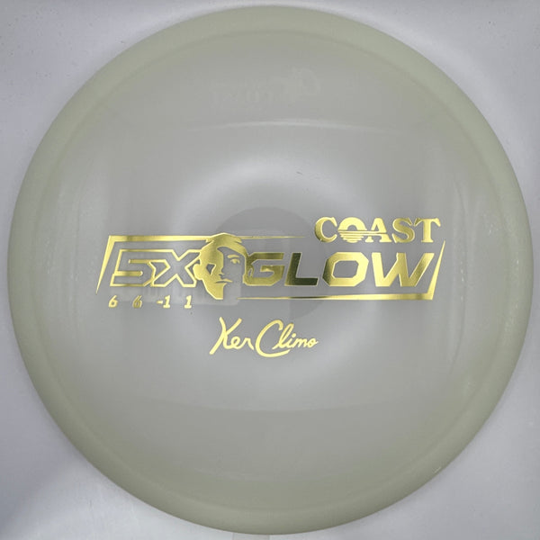 A translucent pale yellow-green Coast Glow disc golf disc with gold foil stamping, shown inside its white packaging box.