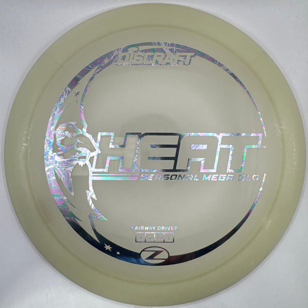 A disc golf disc, specifically a Nitzsche Heart model, in a translucent pale cream color with holographic silver foil graphics, resting on its white cardboard packaging.