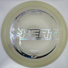 A disc golf disc, specifically a Nitzsche Heart model, in a translucent pale cream color with holographic silver foil graphics, resting on its white cardboard packaging.