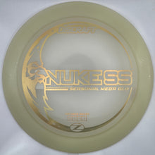 A disc golf disc, specifically the Nukess Zennoral Mebra Elite, in a translucent pale yellow color with gold foil lettering, resting on a white foam insert.