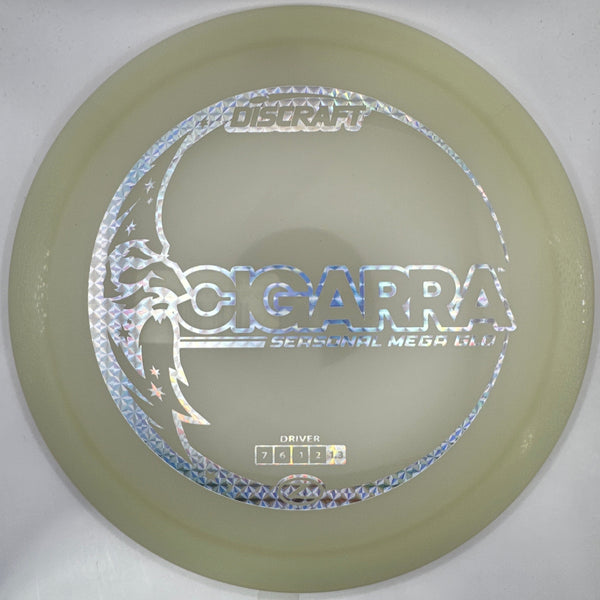 A Discraft Sigurra midrange disc golf disc in a pale yellow-green translucent plastic, featuring a silver holographic foil stamp with the Discraft logo and a dragon graphic, shown inside its white protective packaging sleeve.