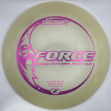 A Discraft Force seasonal meta glo disc golf disc in translucent pale yellow with a metallic purple foil stamp, shown inside its white packaging box.