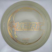 A translucent pale green disc golf disc with gold foil graphics, including the text 'HEAT' and 'SERIAL MEDLEY 2024', displayed inside its white protective packaging sleeve.