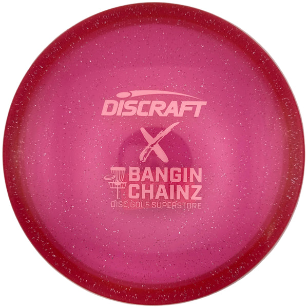 A pink Discraft X Bangin' Chainz disc golf disc with a glittery finish, displayed on a white surface.