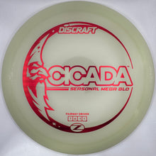 A Discraft Scada Seasonal Meep Gold disc golf disc resting on white foam packaging, featuring a translucent gold body with red printed graphics.