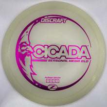 A Discraft Cicada personal mega 6.0 disc golf disc in translucent pale yellow, featuring a vibrant magenta/purple graphic with the model name and wing logo.