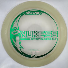 A Discraft Nukess Seasonal Metal Glo disc golf disc in translucent cream with green and black printed graphics, resting on a white foam insert.