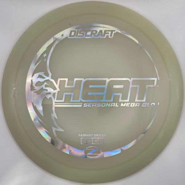 A Discraft Heat Seasonal Mega Ball disc golf disc in translucent pale green, shown inside its white plastic sleeve with a purple disc partially visible on the right.