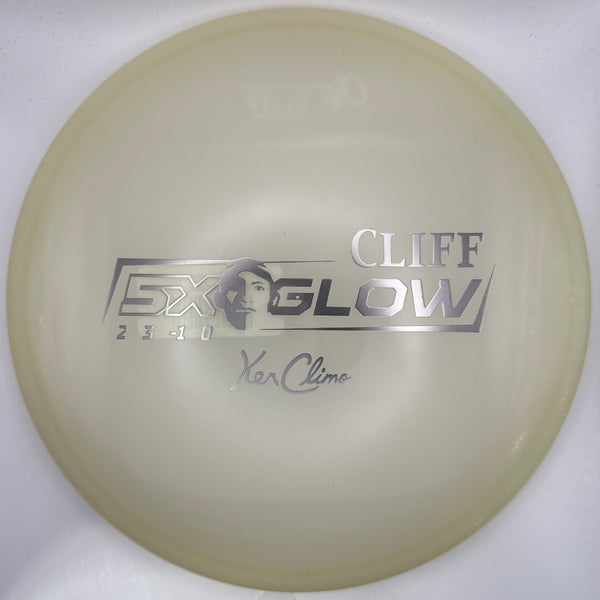 A translucent pale yellow disc golf disc with silver foil stamping that reads 'CLIFF GLOW' and 'Yan Klem' on a white backing card.