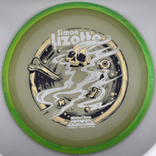 A disc golf disc from the MVP Whiskey Tree Series, featuring a green translucent rim and a light olive-green flight plate with a gold and black graphic of a skull, smoke, and a bone. The text 'Simon Lizotte' is printed on the top.
