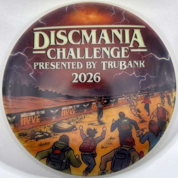 A circular Discmania Challenge 2026 commemorative pin or medallion featuring a split design with a dark stormy landscape on the left and an illustrated desert scene with figures on the right. Text on the left reads 'DISCMANIA CHALLENGE', 'PRESENTED BY TRUBANK', and '2026'.