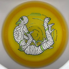 A yellow disc golf disc with a graphic of a mummy wrapped in bandages, featuring the MVP logo and a signature by James Chen.