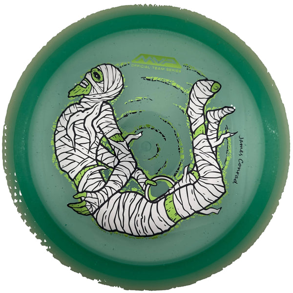 A translucent green disc golf disc featuring a cartoon mummy design with white bandages and lime green accents, photographed from directly above inside a circular opening.