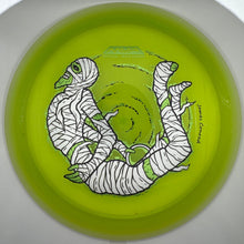 A lime green disc golf disc featuring a black and white illustration of a mummy wrapped in bandages, photographed from directly above inside its white circular packaging.