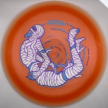 An orange translucent disc golf disc featuring a white and blue illustrated design of two wrapped figures, photographed inside a circular opening.